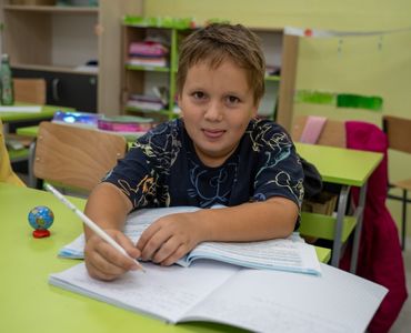 Nasmejani učenik piše u svesku na času