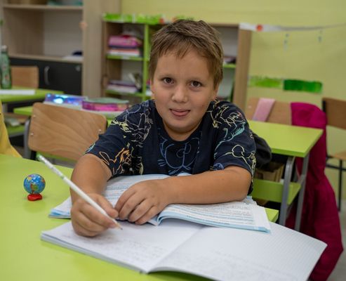 Nasmejani učenik piše u svesku na času